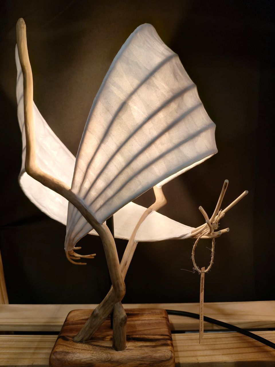 El abrazo: dos alas de papel abiertas sobre ramas de madera, iluminadas desde adentro