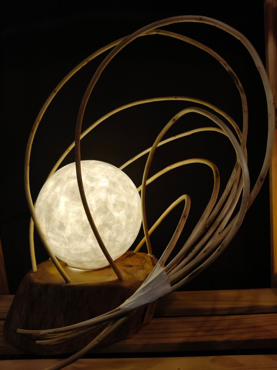 Esfera luminosa rodeada de aros de bambú en espiral sobre base de madera